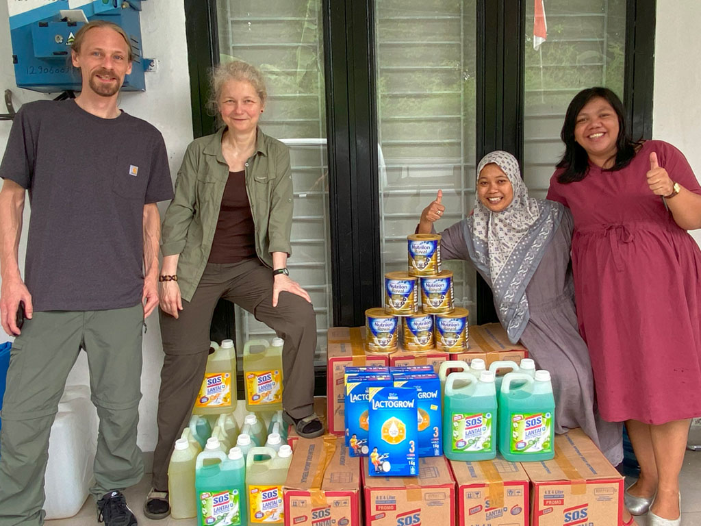 Übergabe von Milchpulver und weiteren Spenden. Zwei Vereinsmitglieder und zwei indonesische Helfer blicken freundlich in die Kamera.