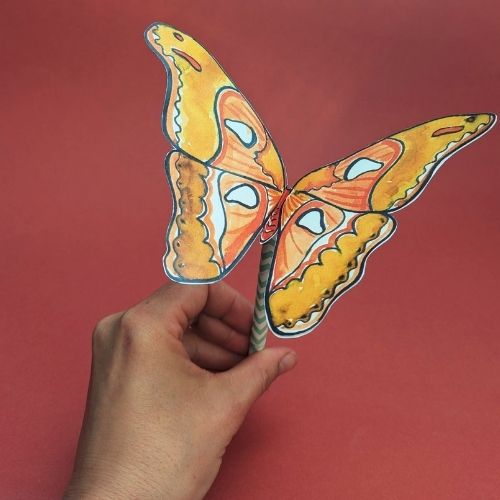 Vor einem roten Hintergrund hält eine Hand einen selbstgebastelten Schmetterling.