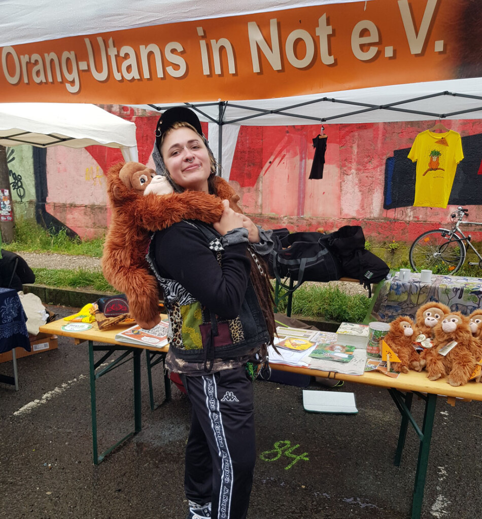 Eine Besucherin steht vor unserem Infostand. Mit einen großen Plüsch-Orang-Utan auf ihrem Rücken lächelt sie in die Kamera.