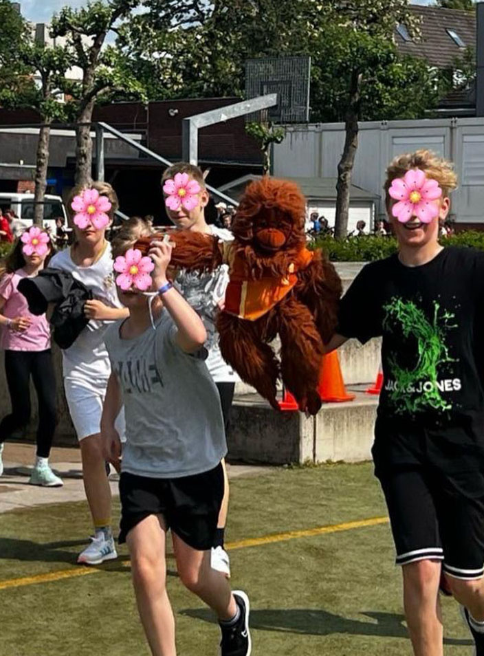 Eine Gruppe Schülerinnen und Schüler laufen auf einem Sportplatz. Ein Junge trägt eine Orang-Utan-Handpuppe.