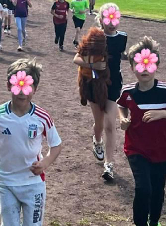 Eine Gruppe Schülerinnen und Schüler laufen auf einem Sportplatz. Ein Mädchen trägt eine Orang-Utan-Handpuppe.