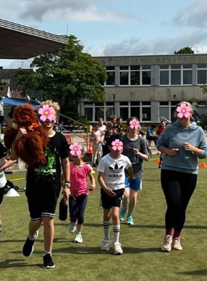 Eine Gruppe Schülerinnen und Schüler laufen auf einem Sportplatz. Ein Junge trägt eine Orang-Utan-Handpuppe.