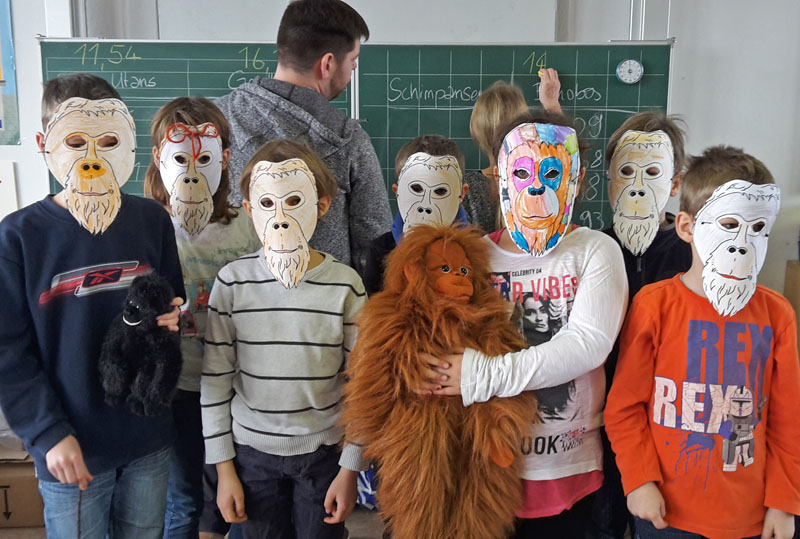 Group photo: A group of elementary school students with homemade orangutan masks in the classroom.