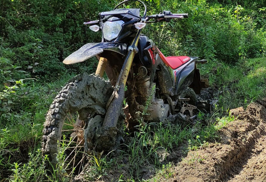 Ein Motorrad steckt auf einer Schlammpiste tief im Matsch.