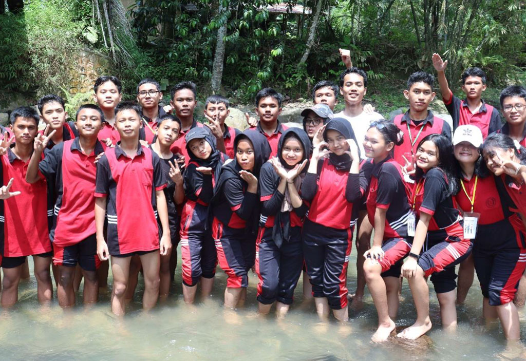 Eine Schulklasse steht Barfuß in einem Fluss und posiert für ein Gruppenfote.