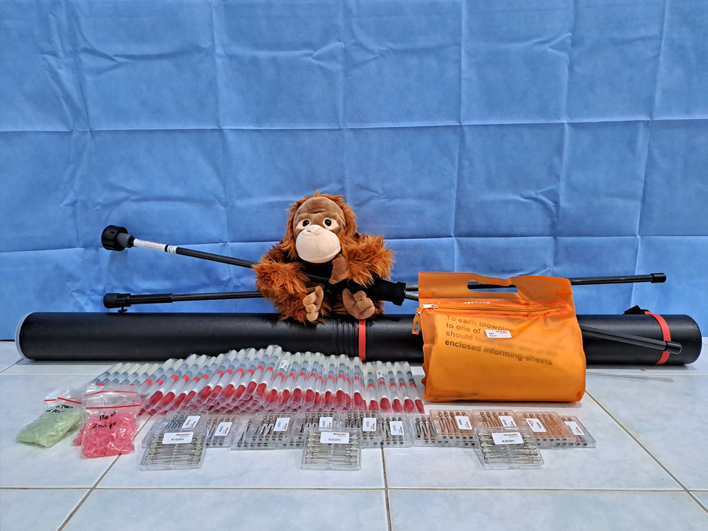 Ein Plüsch-Orang-Utan sitzt hinter hinter diversen Ausdrüstungsteilen für Blasrohre.
