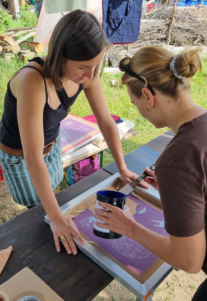 Eine Besucherin an unserem Stand bedruckt ein T-Shirt: Sie trägt Farbe auf die Siebdruckvorlage auf. Eine Mitarbeiterin des Vereins unterstützt sie.