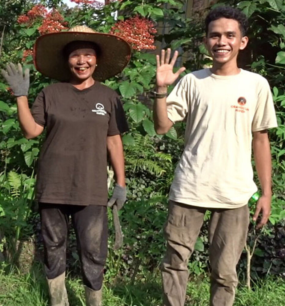 Zwei Mitarbeiter des Farming Centers des Orangutan Haven winken fröhlich in die Kamera.
